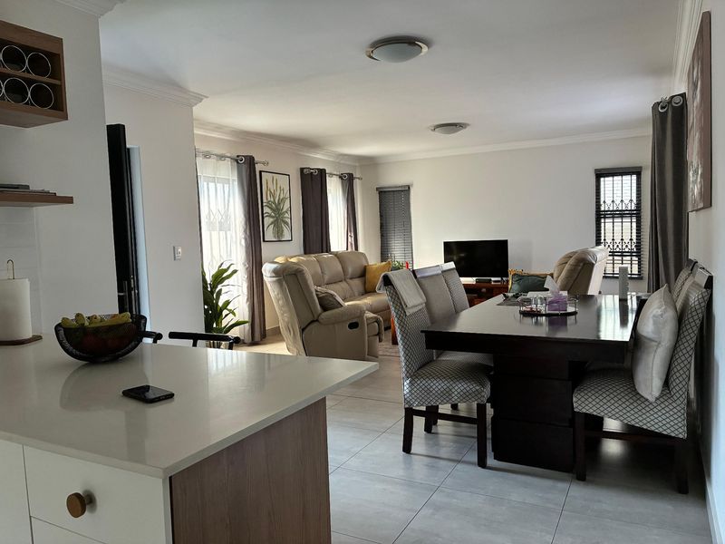Spacious open-plan living and dining area featuring tiled flooring, a modern kitchen island with stone countertops, and ample natural light through multiple windows.