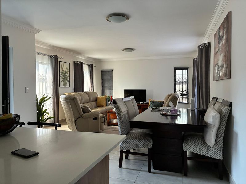 Spacious open-plan living and dining area featuring tiled flooring, neutral walls, and natural light through multiple windows with security bars.