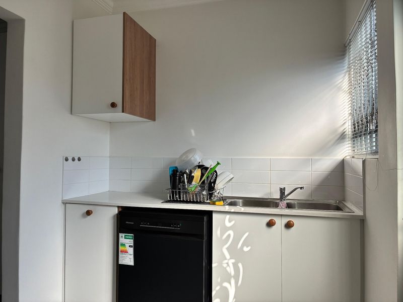 A functional scullery area featuring built-in cabinetry, a stainless steel sink with mixer tap, and tiled splashback, providing additional workspace and utility.