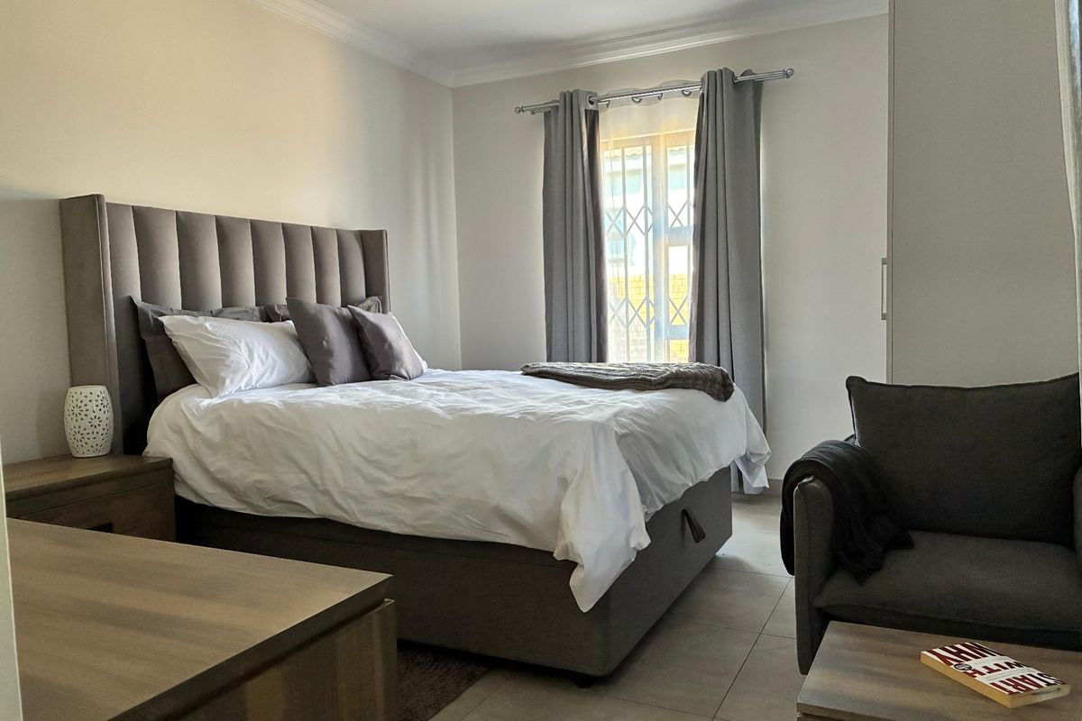 A well-maintained bedroom featuring neutral tiled flooring, a built-in wardrobe, and a security gate on the window for added peace of mind.