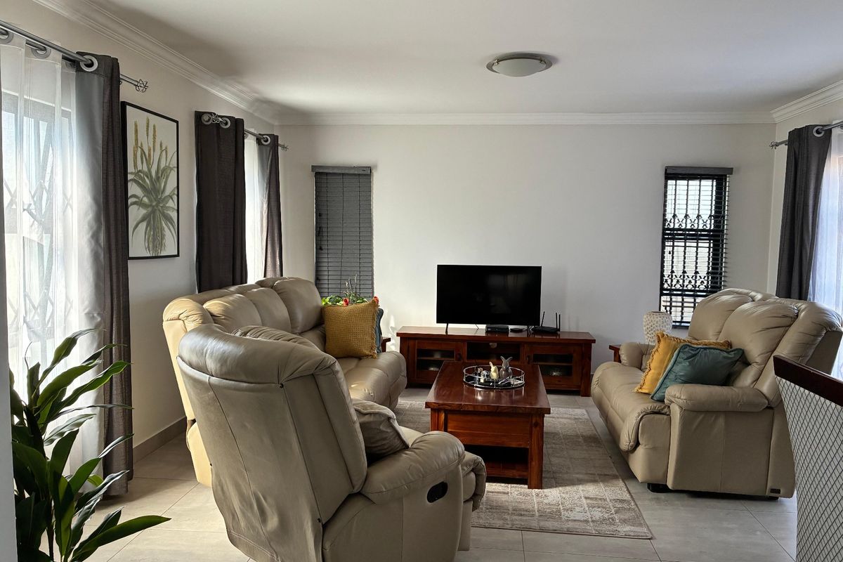 A well-maintained living room featuring tiled flooring, neutral walls, cornicing, and security gates on the windows.