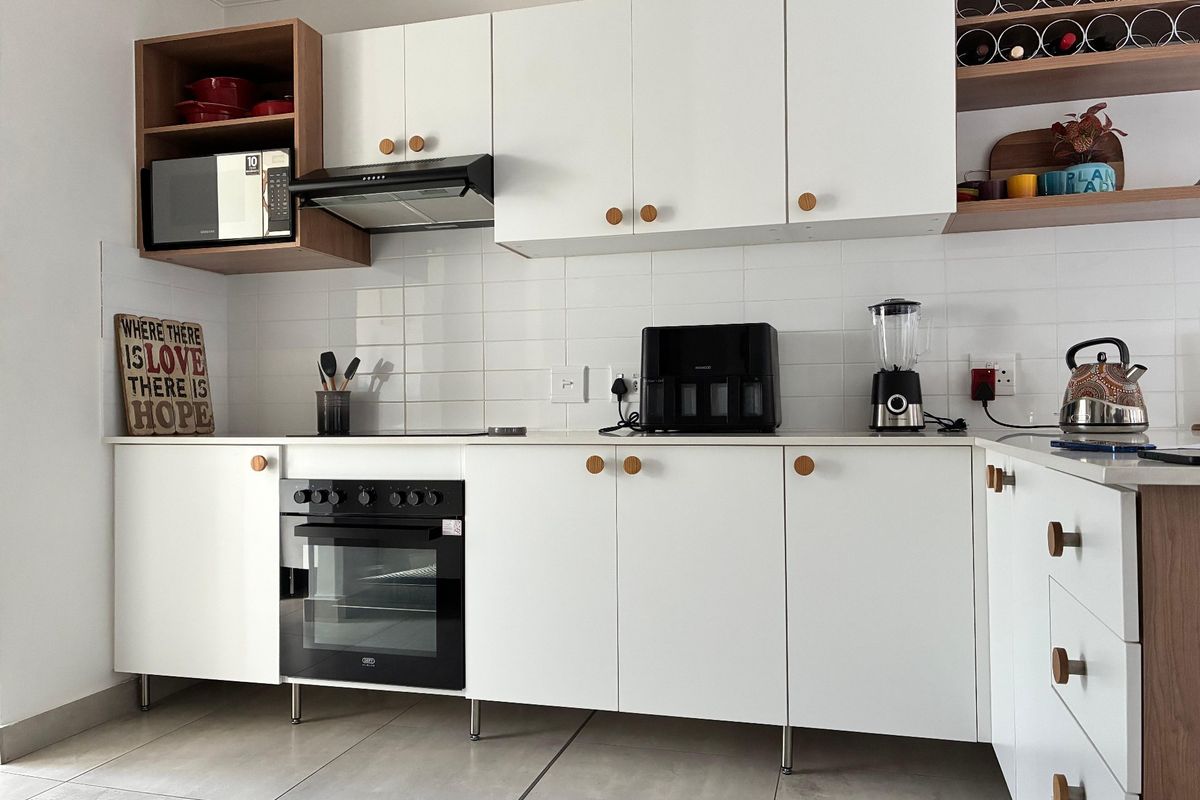 Modern kitchen featuring white cabinetry, built-in oven, extractor fan, integrated microwave, and tiled splashback with contemporary wood-accented open shelving.