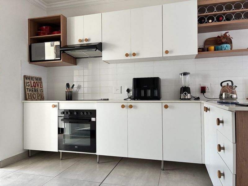 Modern kitchen featuring white cabinetry, built-in oven, extractor fan, integrated microwave, and tiled splashback with contemporary wood-accented open shelving.