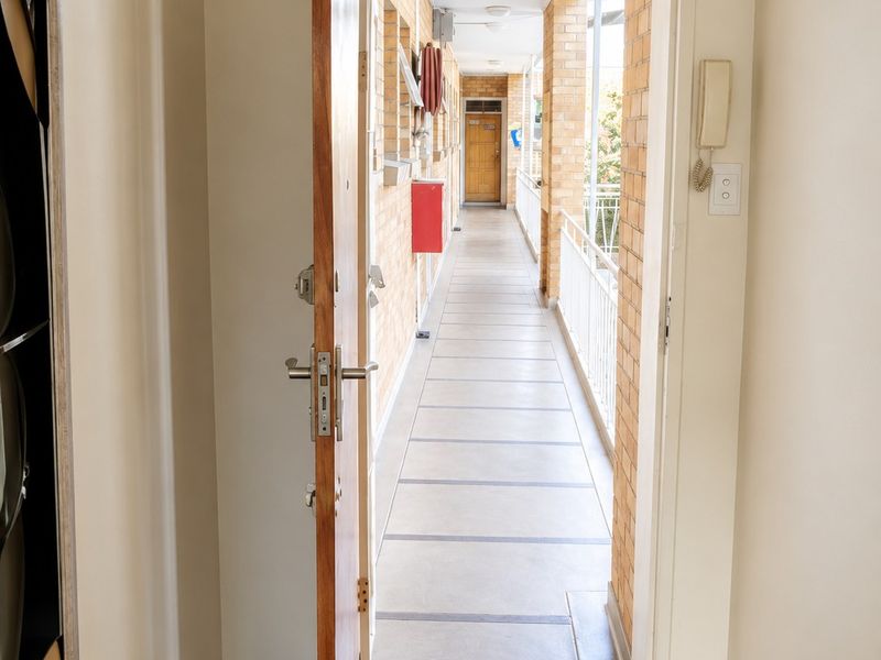 View from the apartment entrance looking out onto an external brick-walled walkway with metal railings and an intercom system installed.
