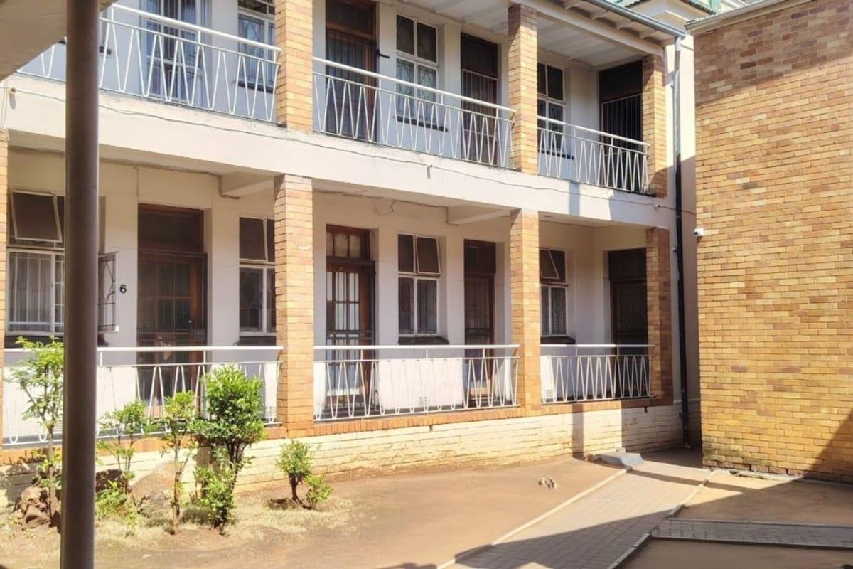 Exterior view of a multi-story apartment building featuring brick facade, metal balcony railings, and shared concrete walkways.