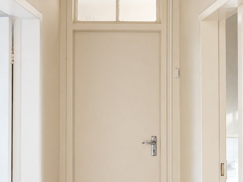 A clean, neutral-toned hallway featuring a central internal door with a transom window and ceiling ventilation.