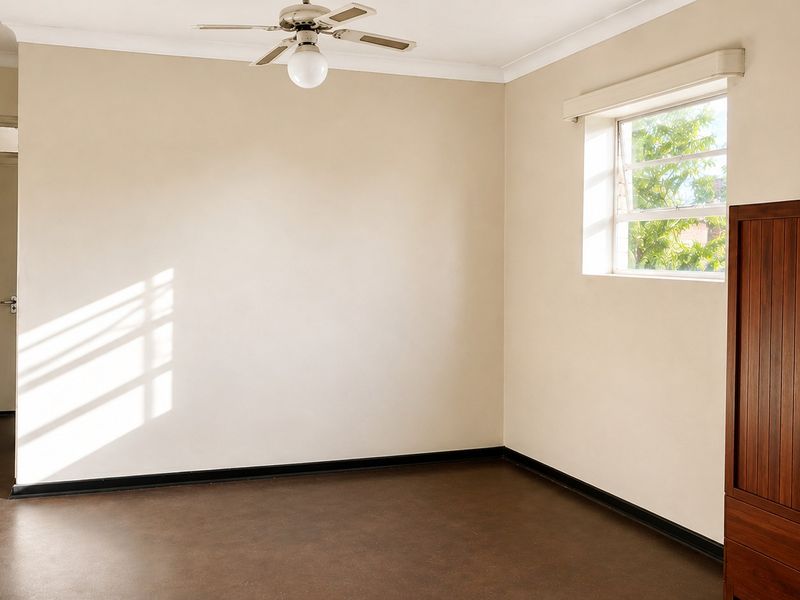 A bright, empty bedroom featuring a ceiling fan, neutral walls, and dark flooring, offering a blank canvas for personalization.