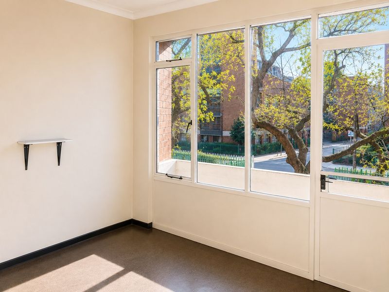 A bright, empty bedroom featuring large windows and a glass door providing natural light and views of the surrounding neighborhood.