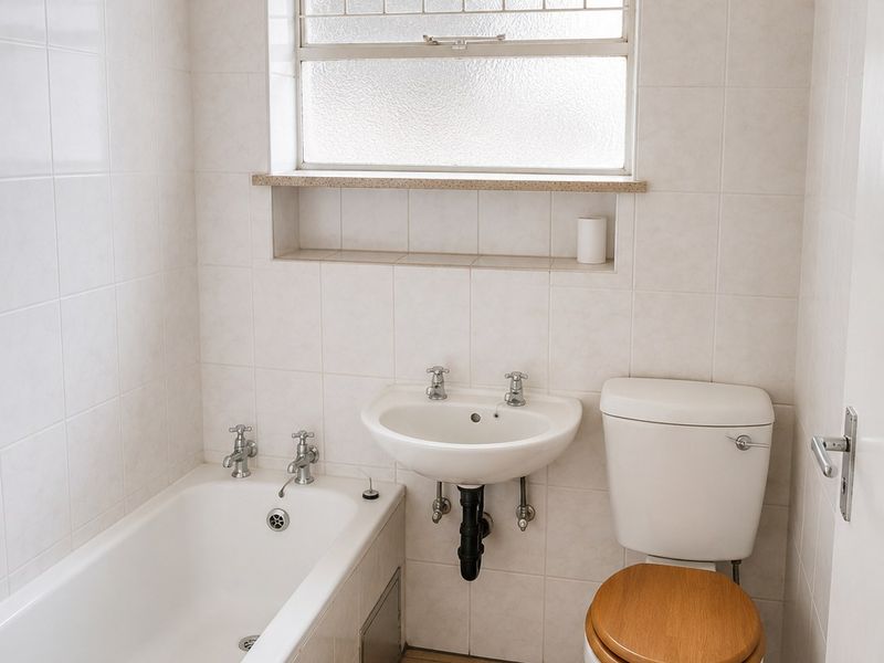 A functional bathroom featuring a bathtub, wall-mounted basin, and toilet, finished with neutral wall tiles and floor tiling.