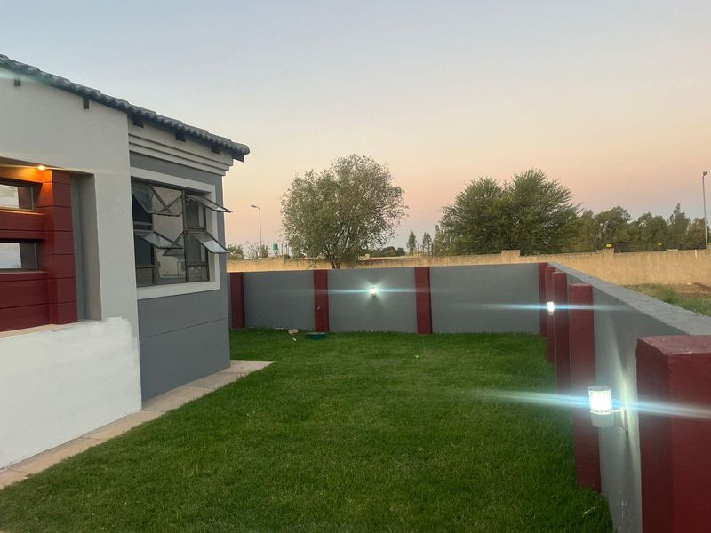 A well-maintained rear garden area featuring a manicured lawn, perimeter boundary wall with integrated lighting, and modern exterior finishes.