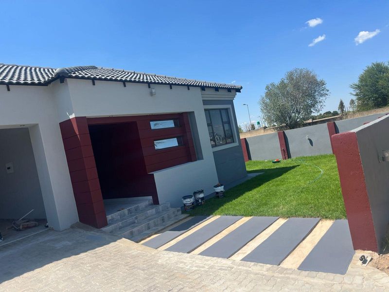 Modern single-story house exterior featuring a tiled roof, paved driveway, concrete walkway, and a well-maintained lawn with a boundary wall.