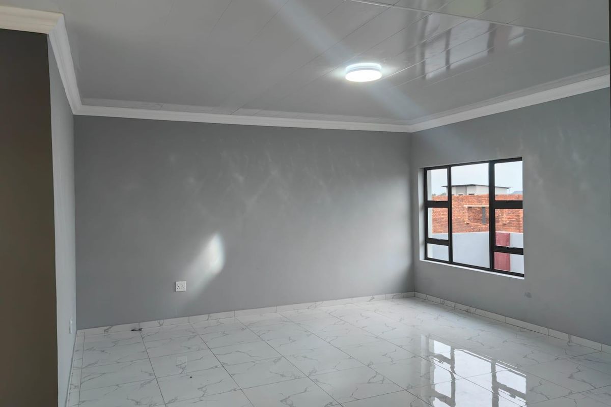 A bright, empty living room featuring modern white marble-look floor tiles, grey walls, and large aluminium-framed windows.
