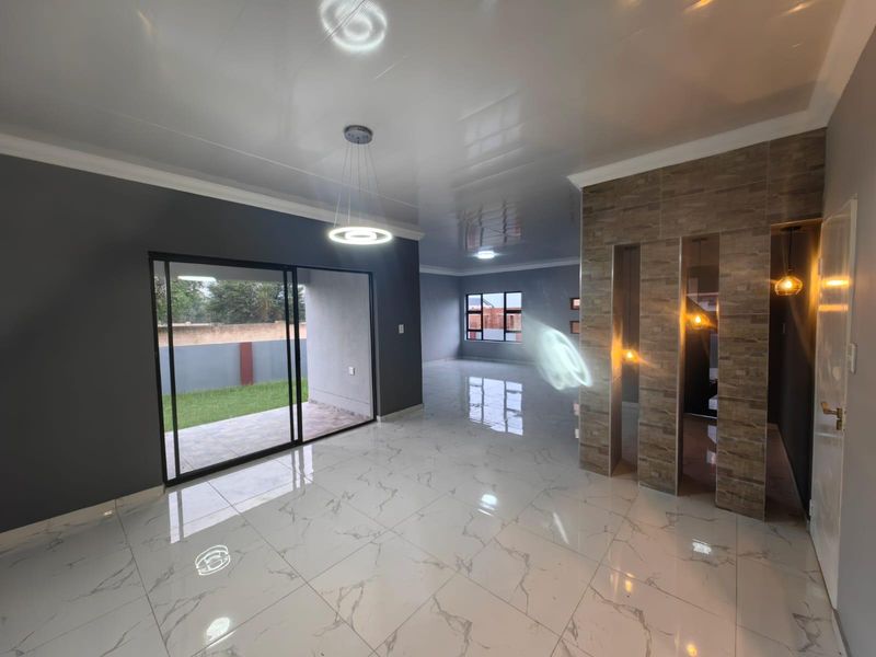Spacious open-plan living area featuring high-gloss marble-look floor tiles, a stone-clad feature wall, and large sliding glass doors leading to the garden.