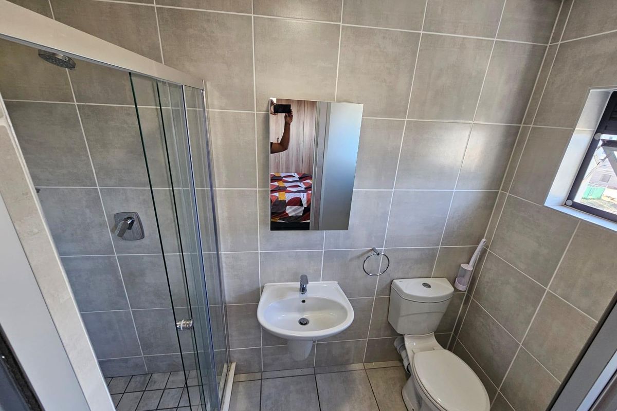 A clean, modern bathroom featuring a glass-enclosed shower, wall-mounted basin, and toilet with neutral floor-to-ceiling tiling.