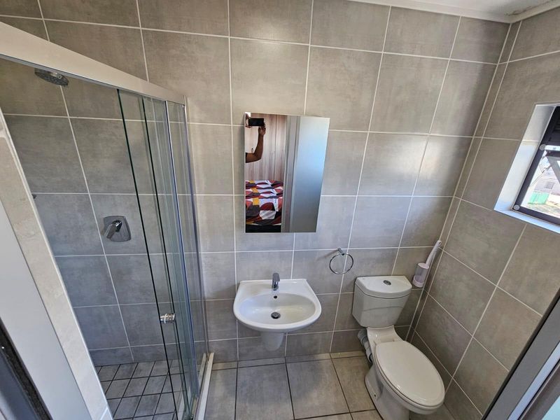 A clean, modern bathroom featuring a glass-enclosed shower, wall-mounted basin, and toilet with neutral floor-to-ceiling tiling.