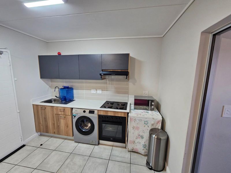 Compact kitchen featuring modern wood-grain and dark grey cabinetry, tiled backsplash, integrated oven, hob, and extractor fan with tiled flooring.