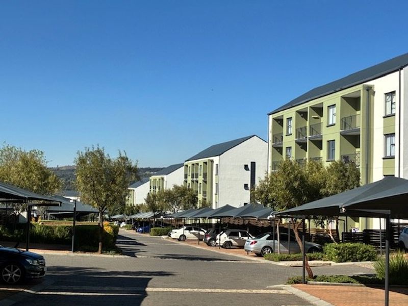 Exterior view of a modern apartment complex featuring paved driveways, covered parking bays, and multi-story residential buildings with balconies.