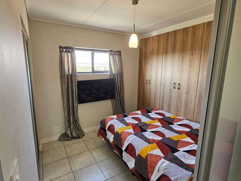 A compact bedroom featuring built-in wooden cupboards, tiled flooring, and a pendant light fixture, offering a functional and tidy living space.