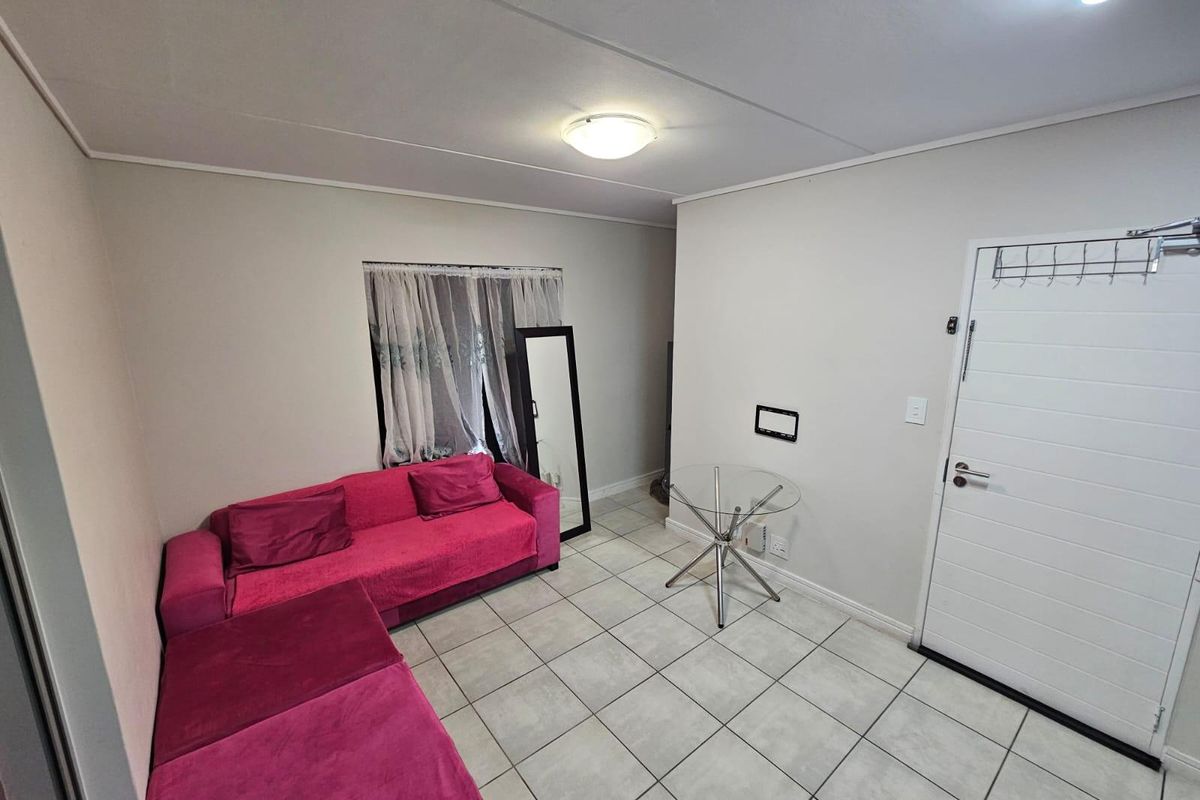A functional living area featuring neutral wall tones, tiled flooring, and a white panel entrance door with overhead lighting.