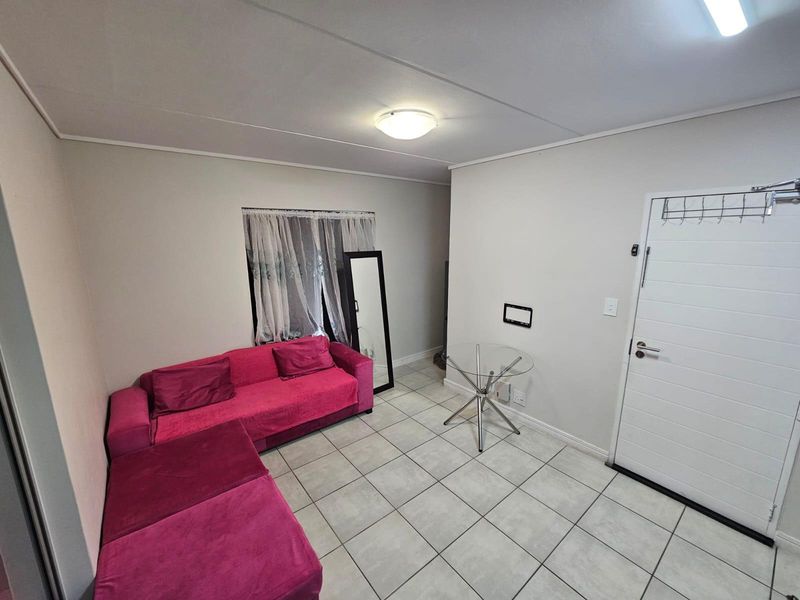 A functional living area featuring neutral wall tones, tiled flooring, and a white panel entrance door with overhead lighting.