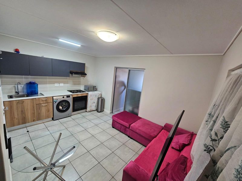 Open-plan living area featuring a compact kitchen with built-in cabinetry, oven, hob, and tiled flooring, leading to a sliding door access.