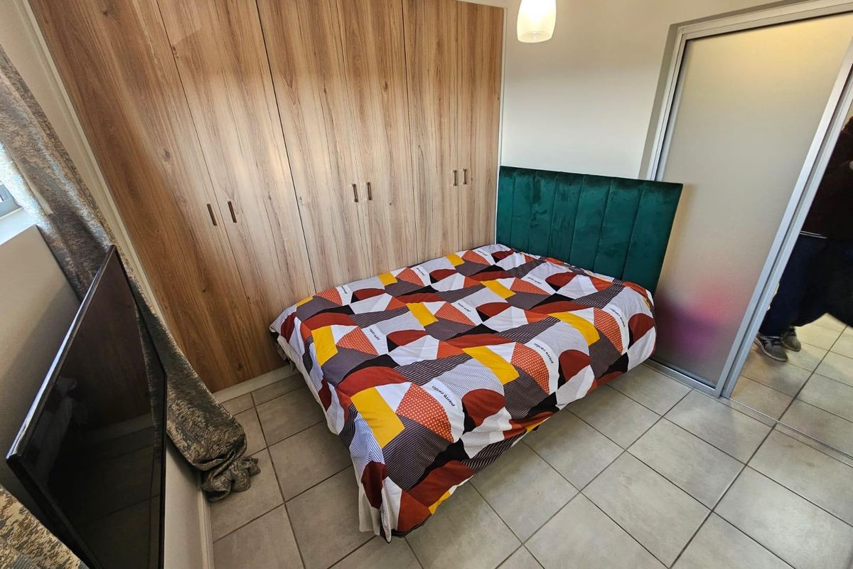 A well-maintained bedroom featuring modern wood-finish built-in cupboards, neutral floor tiles, and a frosted glass door.