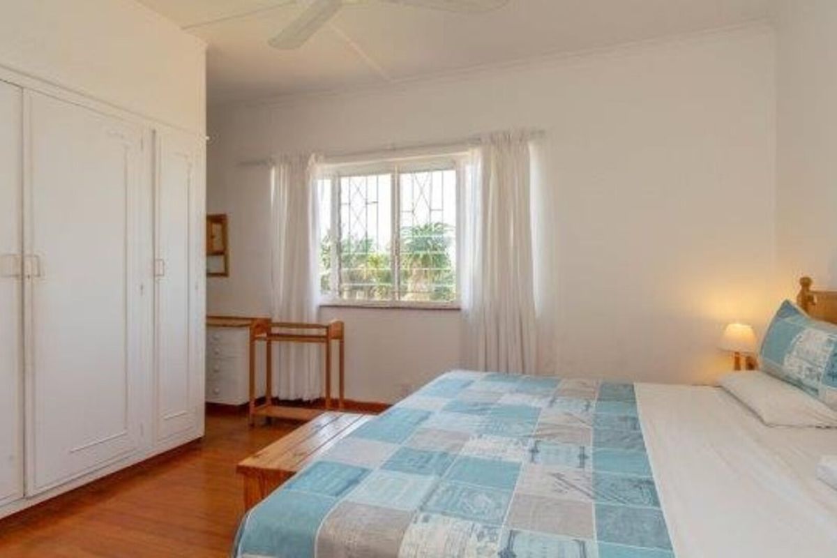 A bedroom featuring wooden flooring, built-in cupboards, a ceiling fan, and a window with security bars.