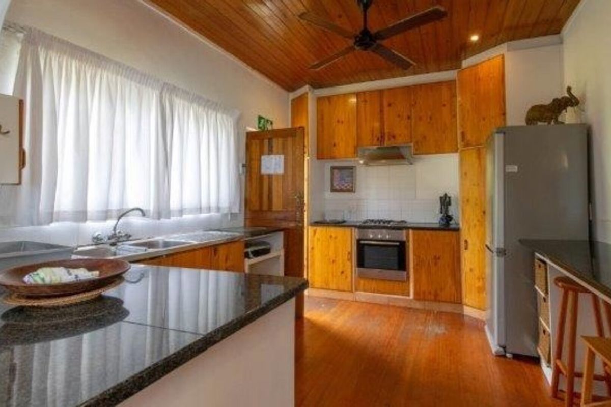 A functional kitchen featuring wooden cabinetry, granite countertops, built-in oven, hob, and a warm wooden ceiling with an integrated fan.