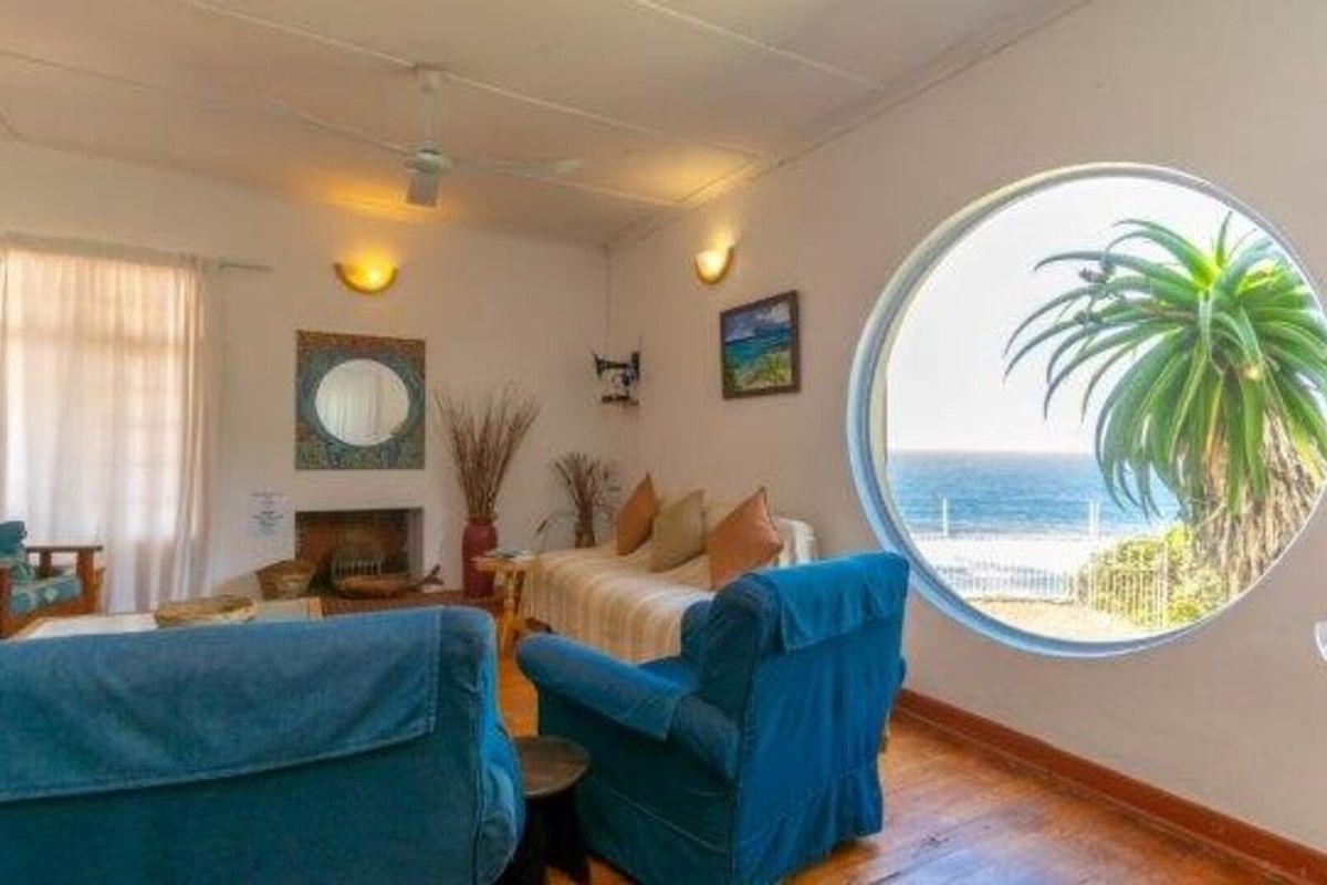 A living room featuring timber flooring, a fireplace, and a distinctive circular window offering scenic ocean views.