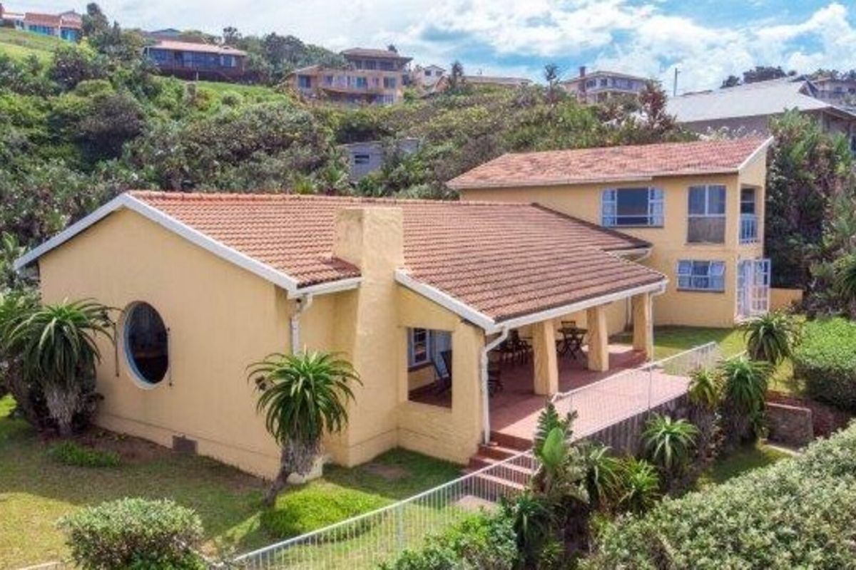 Rear view of a multi-level house featuring a covered patio, terracotta tiled roof, and established garden surroundings.