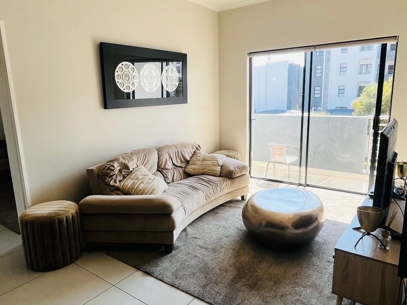 A bright living room featuring large sliding glass doors that open onto a balcony, complemented by neutral tiled flooring and modern ceiling lighting.