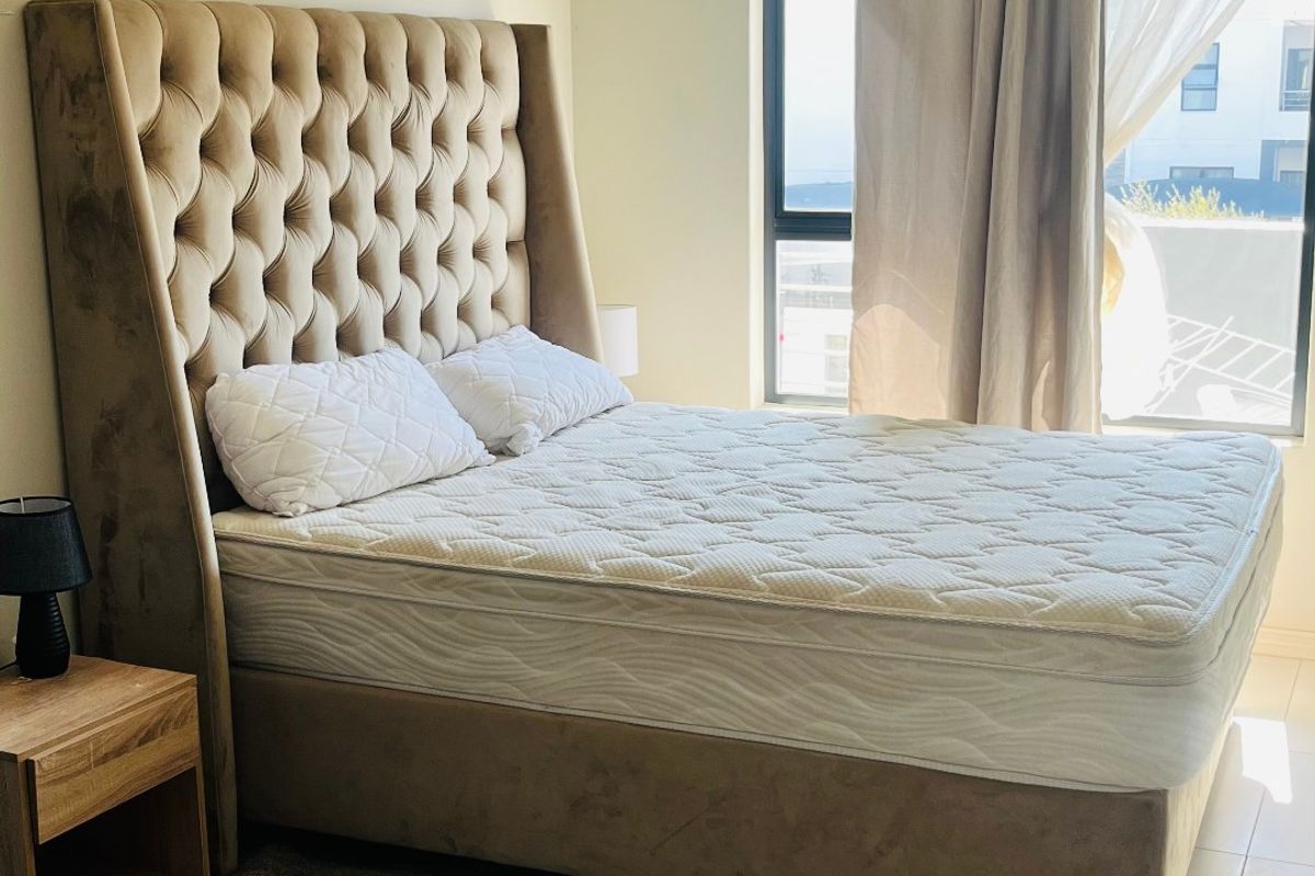 A well-lit bedroom featuring neutral wall tones, tiled flooring, and a large window with installed curtain tracks.