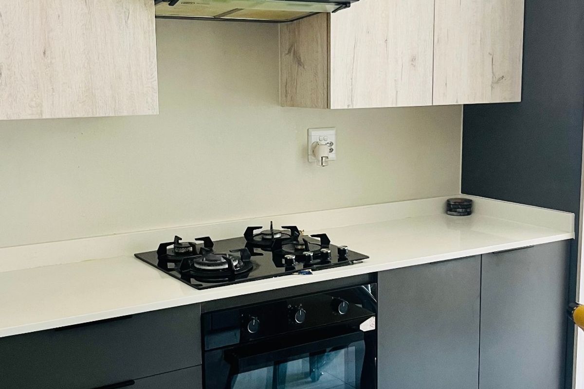 Modern kitchen featuring two-tone cabinetry, stone countertops, a gas hob, built-in oven, and extractor fan with clean tiled flooring.