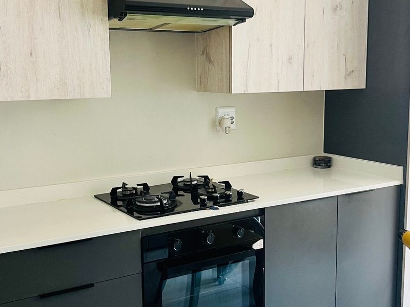 Modern kitchen featuring two-tone cabinetry, stone countertops, a gas hob, built-in oven, and extractor fan with clean tiled flooring.