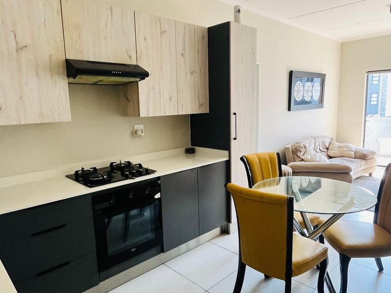 Modern open-plan kitchen featuring two-tone cabinetry, gas hob, and integrated oven, flowing seamlessly into the living area with tiled flooring throughout.