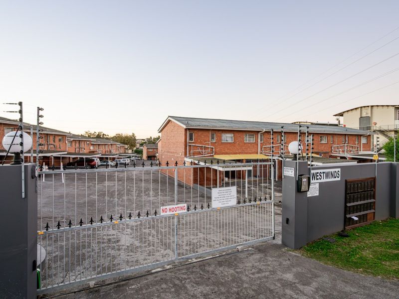 Front entrance view of the Westwinds apartment complex, featuring a secure gated access point, electric fencing, and brick building facades.