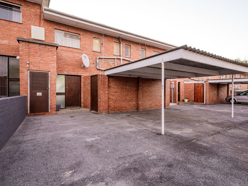 Exterior view of the apartment building featuring a brick facade, covered carport parking, and paved driveway access.