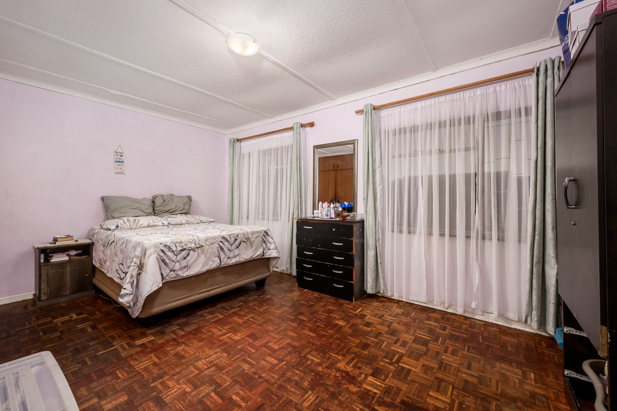 A spacious bedroom featuring traditional parquet flooring, large windows with curtain rods, and a central ceiling light fixture.