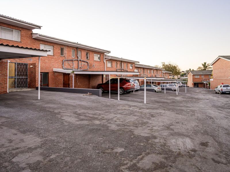 Exterior view of an apartment complex featuring brick facade construction, covered parking carports, and an asphalt driveway area.