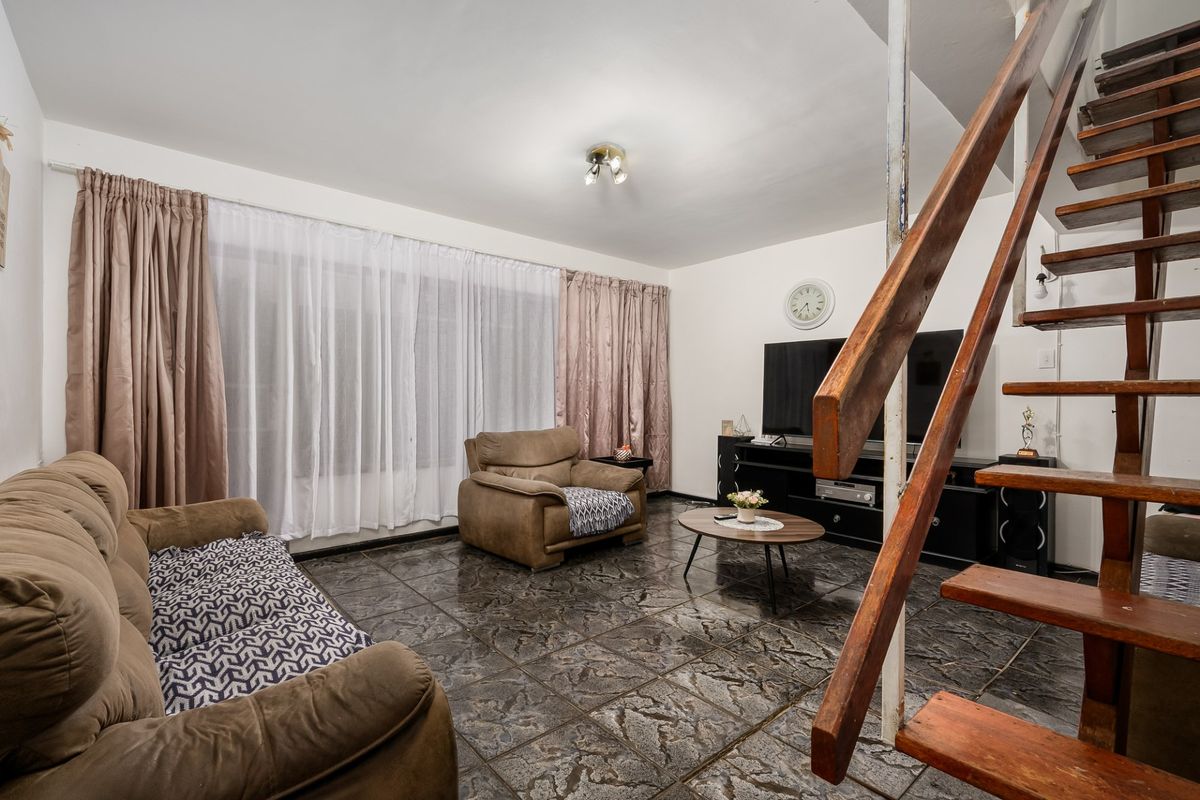A living room featuring dark tiled flooring and an open-tread wooden staircase leading to the upper level.