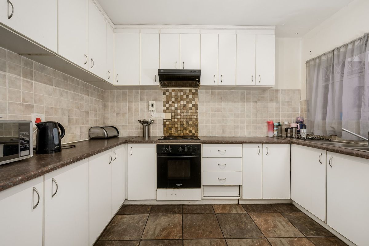Functional kitchen featuring white cabinetry, tiled backsplash, built-in oven with extractor fan, and dark tiled flooring.