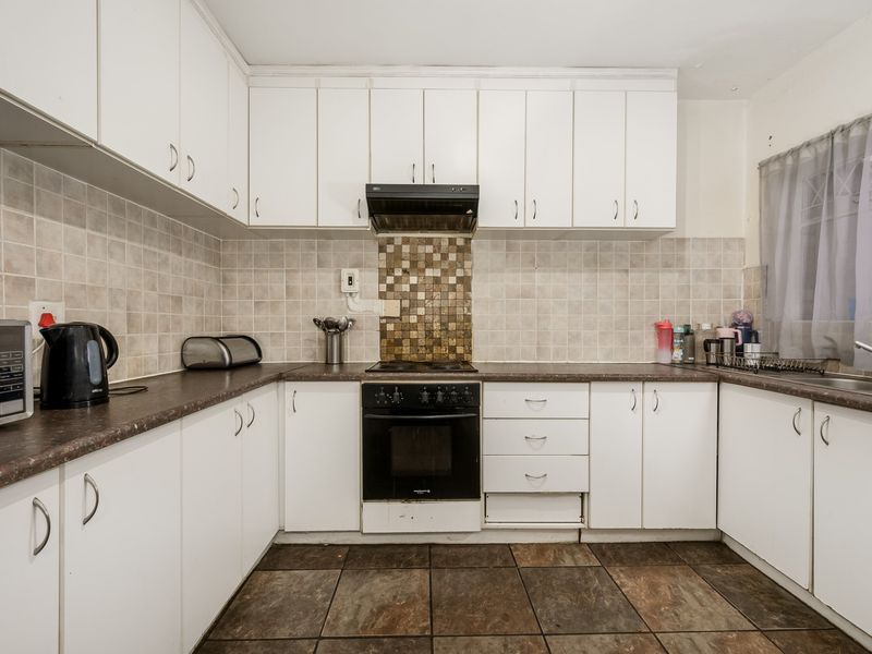 Functional kitchen featuring white cabinetry, tiled backsplash, built-in oven with extractor fan, and dark tiled flooring.