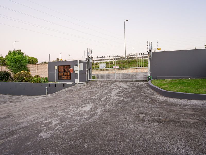 Secure gated entrance to the apartment complex featuring an automated gate, electric fencing, and a paved driveway.