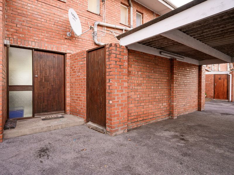 Front entrance area featuring a brick facade, a covered carport, and a timber front door with a concrete threshold.