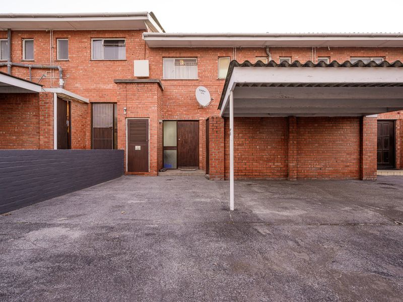Front exterior view of the apartment featuring a brick facade, a covered carport, and an asphalt driveway area.