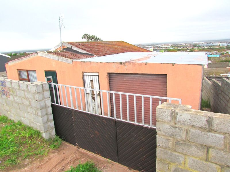 Front exterior view of a residential property featuring a garage with a roller door, perimeter wall, and mixed roofing materials.