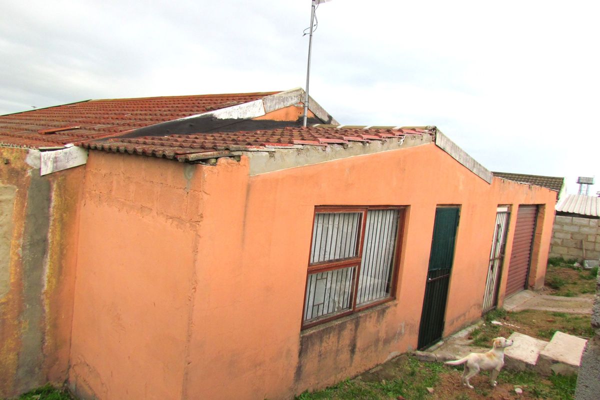 Rear view of the property showing exterior walls, tiled roof, security bars on windows, and a garage door.