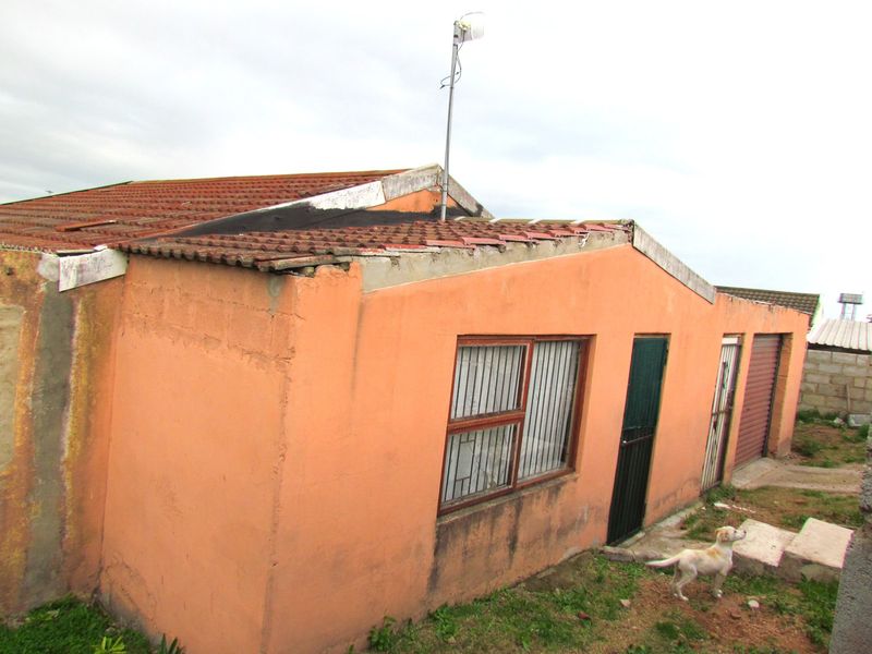 Rear view of the property showing exterior walls, tiled roof, security bars on windows, and a garage door.