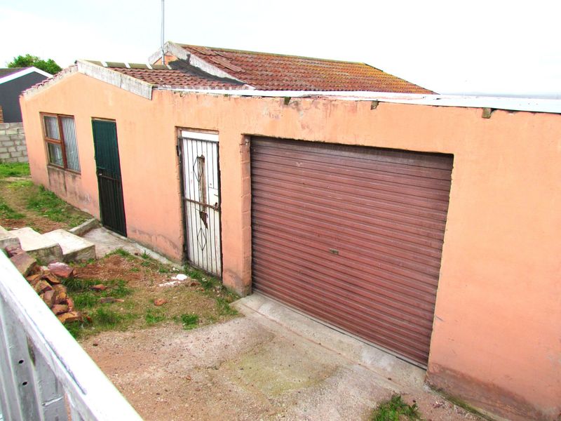 Exterior view of a detached garage featuring a roller shutter door, security gate, and tiled roof showing signs of significant wear and maintenance requirements.