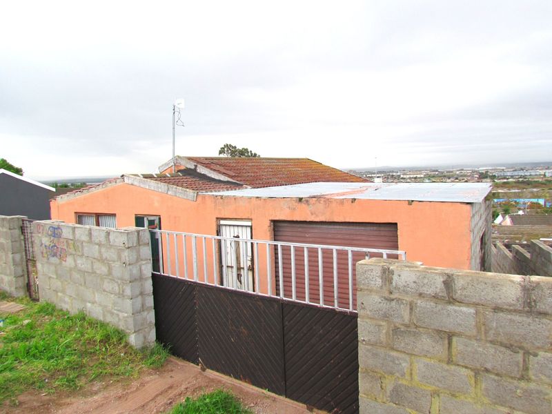 Exterior view of a single-story house featuring a concrete block boundary wall, metal gate, roller garage door, and a combination of tiled and metal roofing.